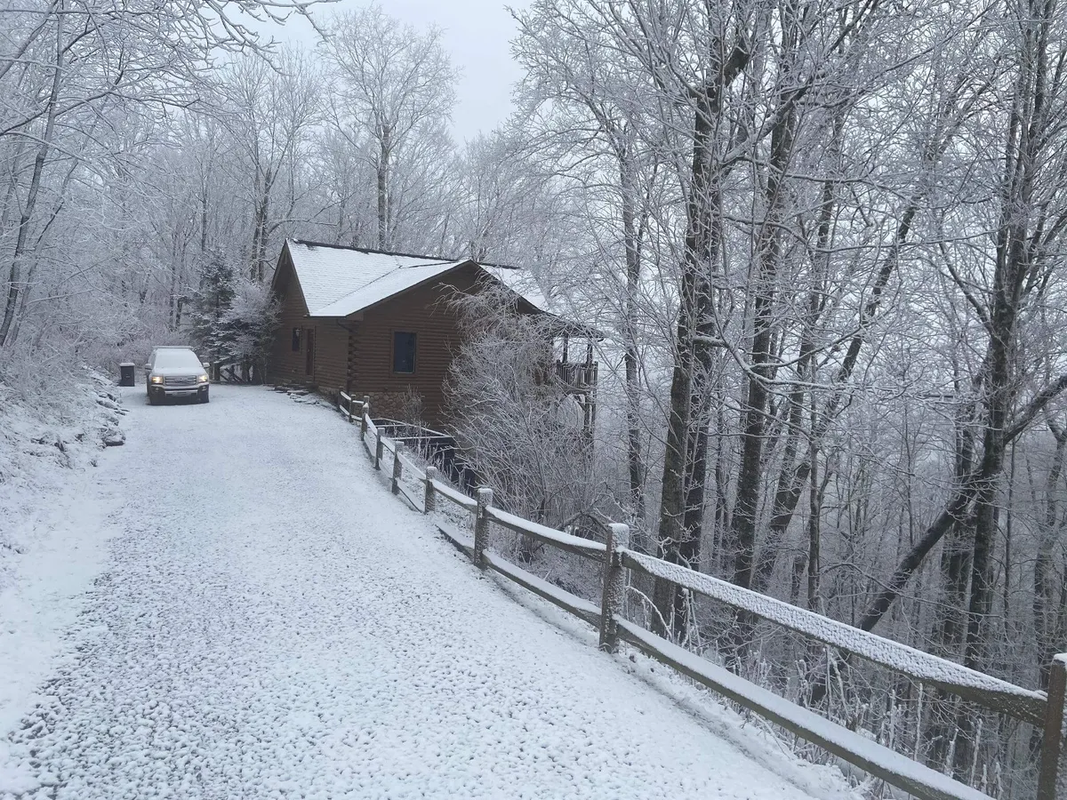 A snow-covered path leads to a charming wooden cabin, surrounded by a fence and winter landscape. The scene is tranquil, inviting visitors to imagine outdoor play and cozy evenings after a day in the mountains.