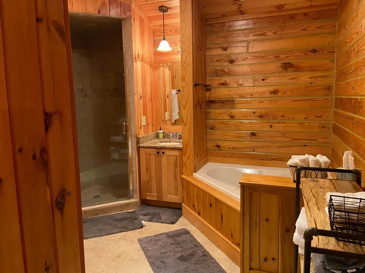 A spacious bathroom featuring both a shower area and a bathtub, with elegant wooden cabinetry and a granite countertop. The space is clean, modern, and designed for relaxation and self-care.