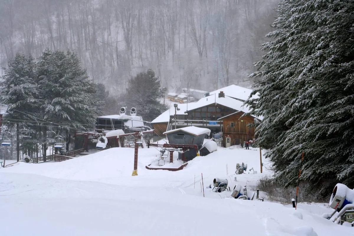 A cozy winter scene showcases snow-covered resort buildings, a ski lift ready for adventure, and tall pine trees in a wintry landscape. The atmosphere is both lively and tranquil, suggesting seasonal activities and communal enjoyment.