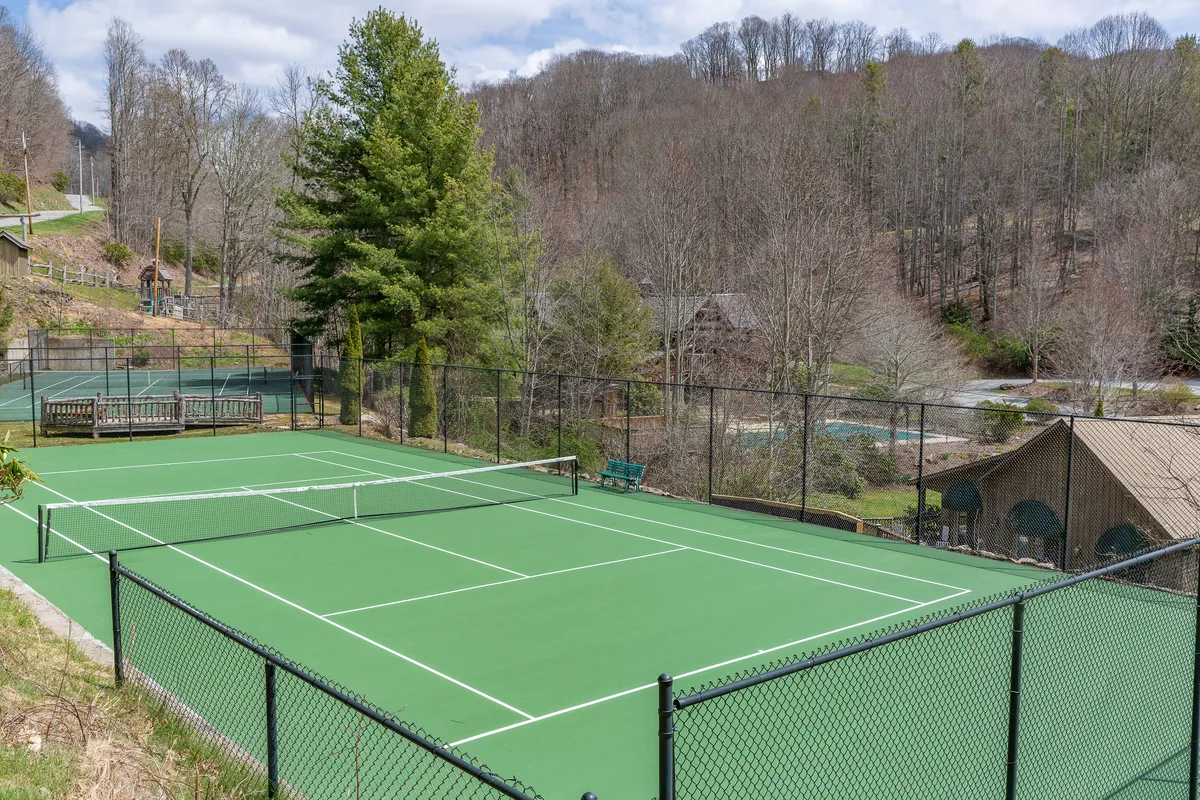 A tennis court surrounded by benches, trees, and distant mountains, set against a serene backdrop that encourages recreation and group play.